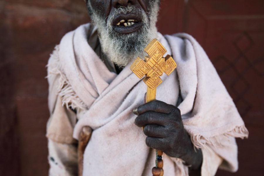 een priester houdt een kruis in de orthodoxe stijl hoog bij zijn kerk in thet
noorden van Eritrea.