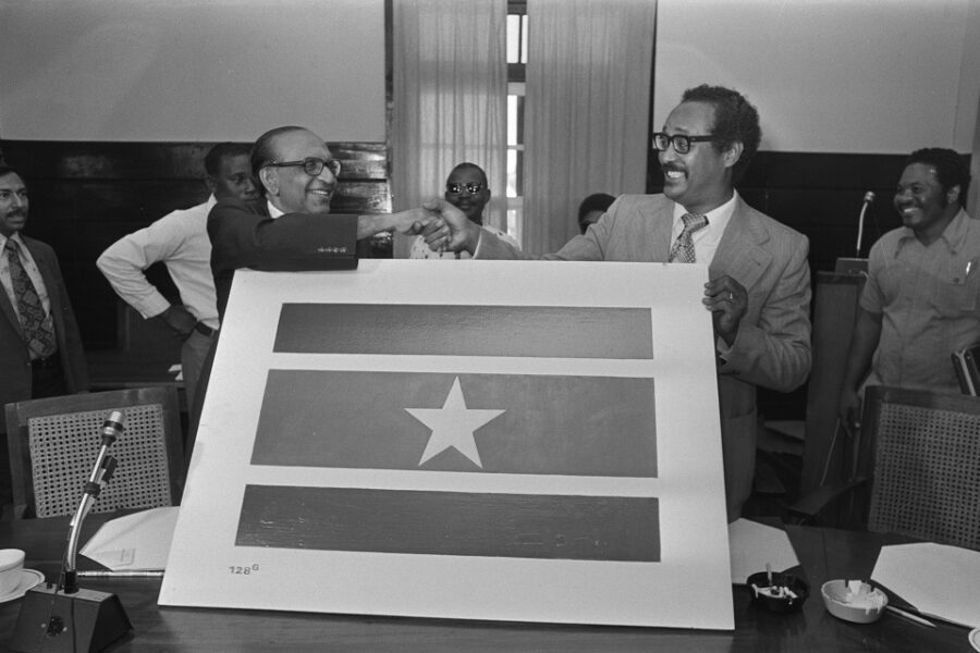Bij de voorbereiding van de onafhankelijkheid stellen premier Arron en
oppositieleider Lachmon de nieuwe Surinaamse vlag voor.